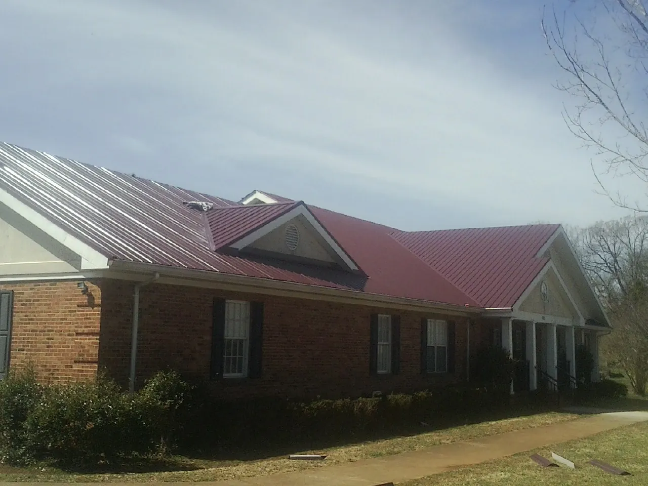 Red metal roof with gabled entries on a long brick building, from a Hail Damage Roof Repair job in Richton Park