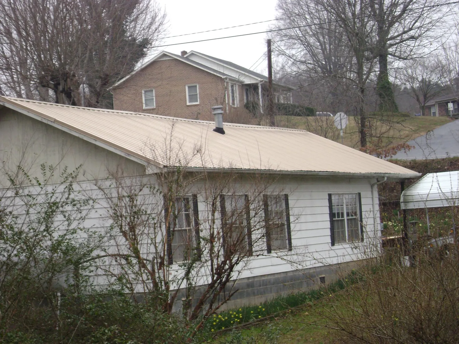 Tan metal roof on a white sided house set into a hillside — Commercial Roofing by Roofing Brothers in Richton Park